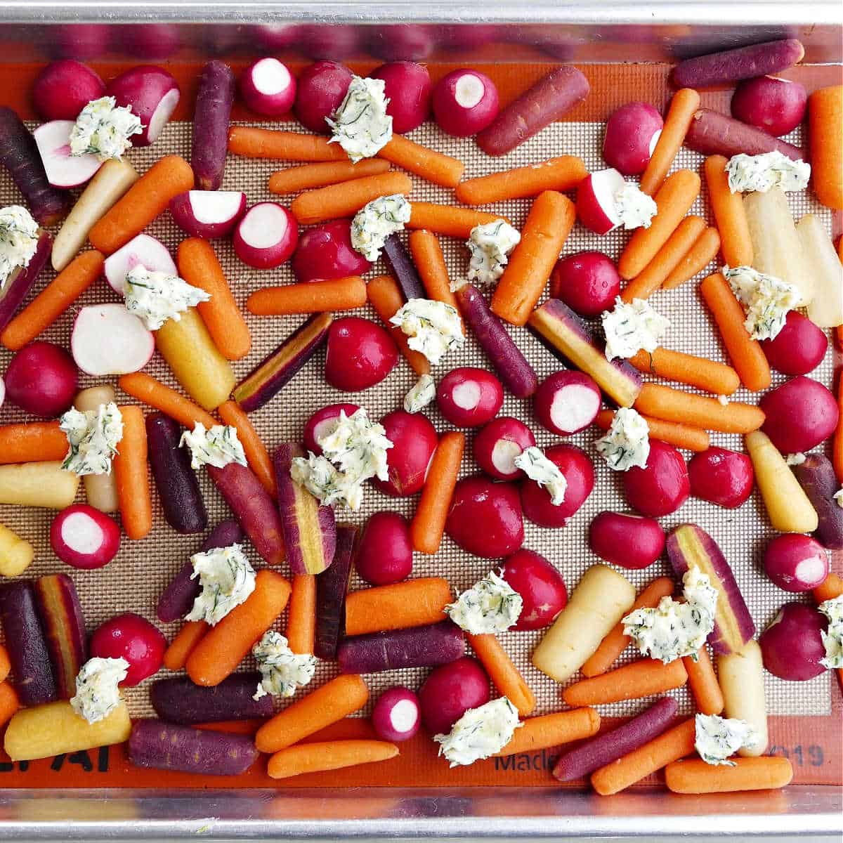 radishes and baby carrots on a baking sheet with dollops of compound butter