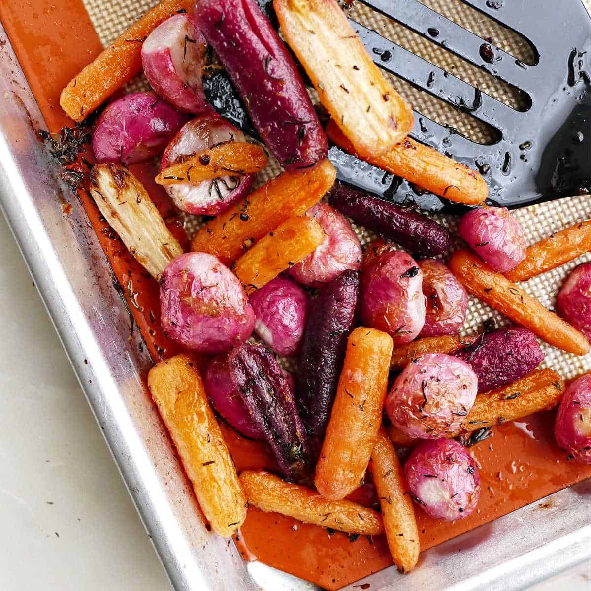 roasted radishes and carrots on a baking sheet with a spatula