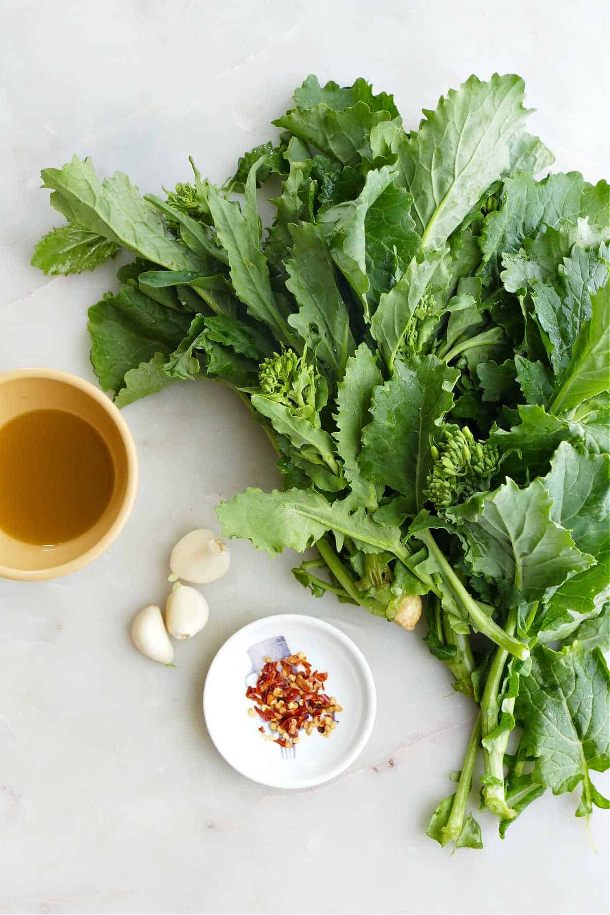 extra virgin olive oil, broccoli rabe, garlic cloves, and red pepper flakes on a counter