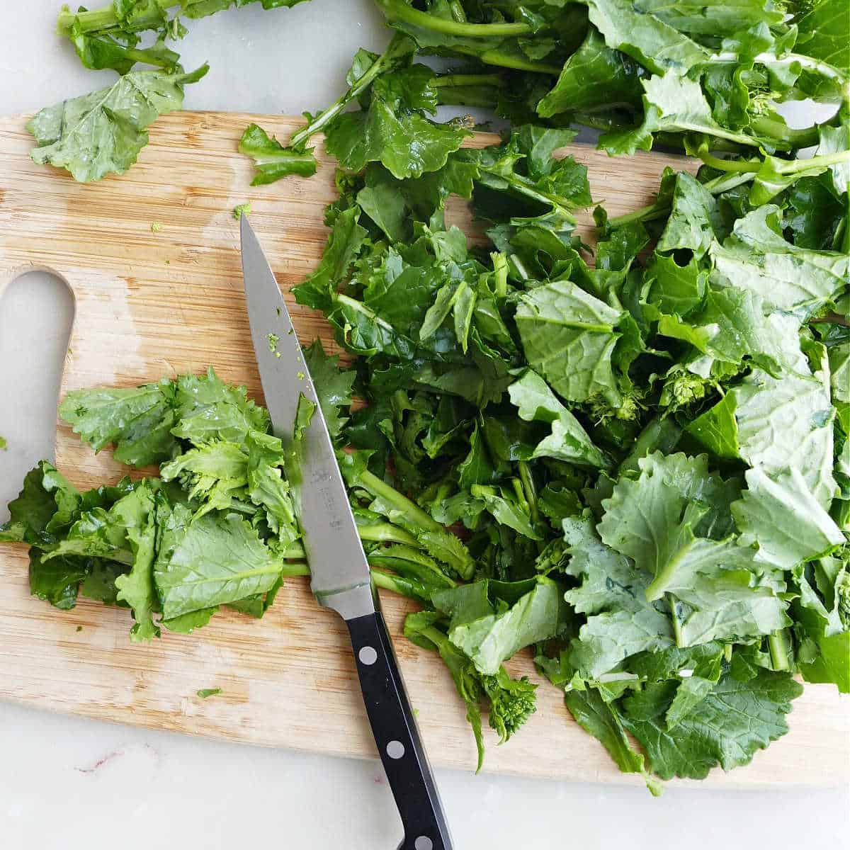 rapini being cut into smaller pieces on a cutting board with a knife