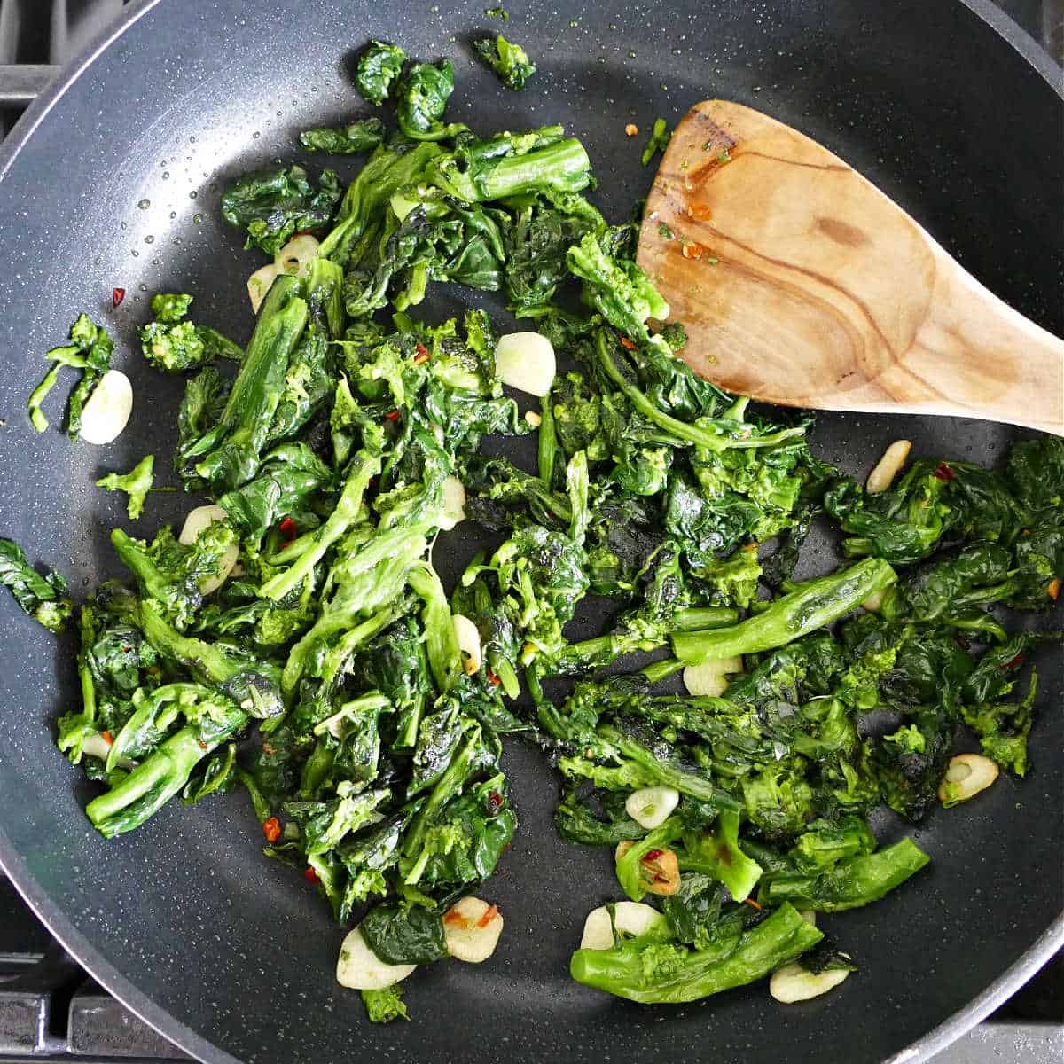 blanched rapini cooking in olive oil with garlic and red pepper flakes in a skillet