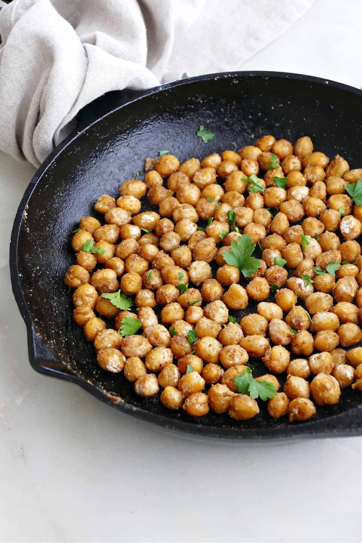 sautéed chickpeas with seasonings in a cast iron skillet with a napkin on the handle
