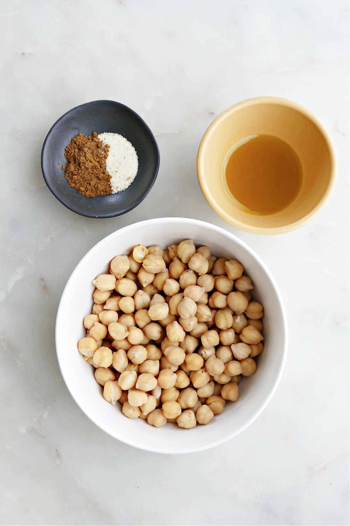 canned chickpeas in a bowl next to olive oil and seasonings on a counter