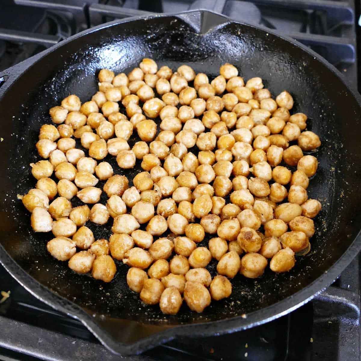 garbanzo beans cooking in olive oil and seasonings in a skillet