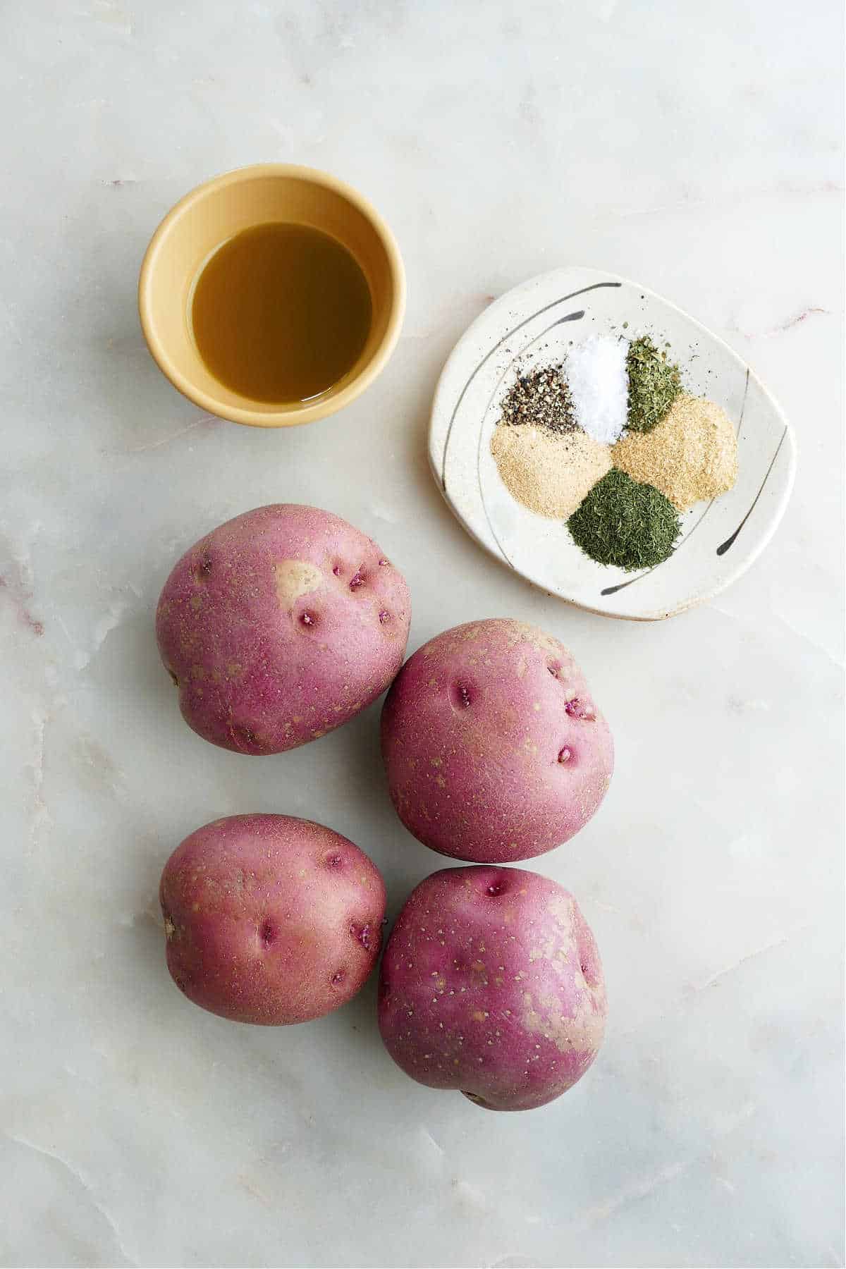 four red potatoes, olive oil, and seasonings on a counter next to each other