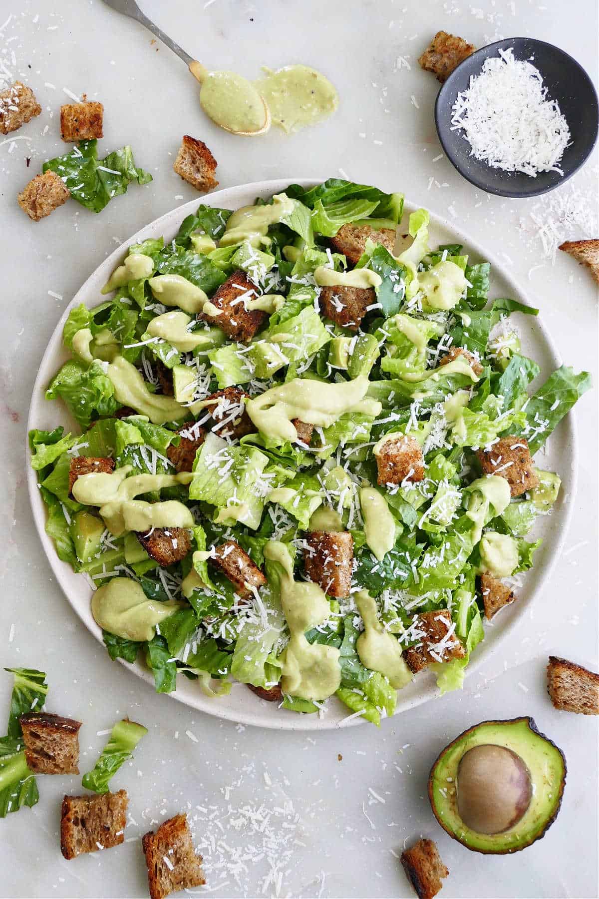 avocado Caesar salad on a large serving plate surrounded by ingredients 