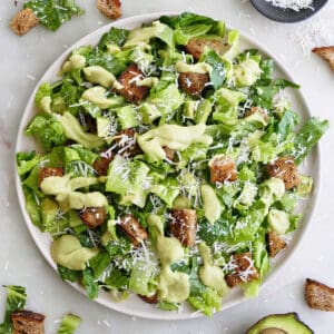 avocado Caesar salad on a large serving plate surrounded by ingredients