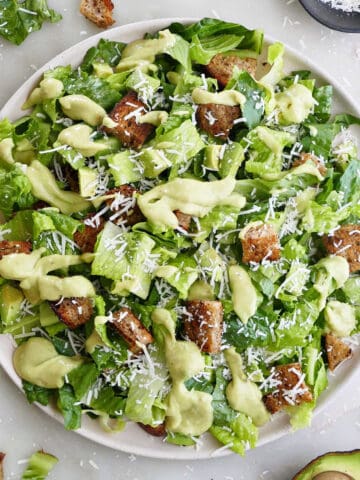 avocado Caesar salad on a large serving plate surrounded by ingredients