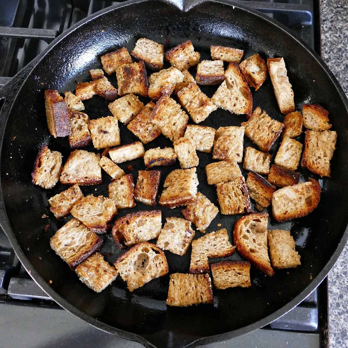 homemade sourdough croutons cooking in olive oil and seasonings in a cast iron skillet