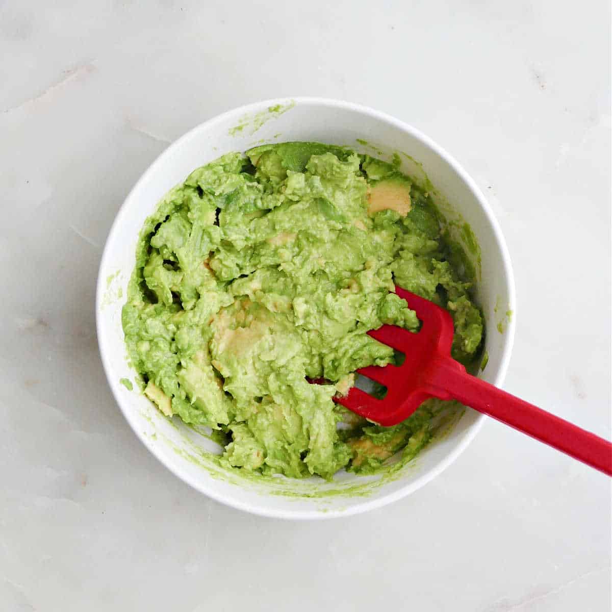 avocado being mashed in a bowl with a silicone fork
