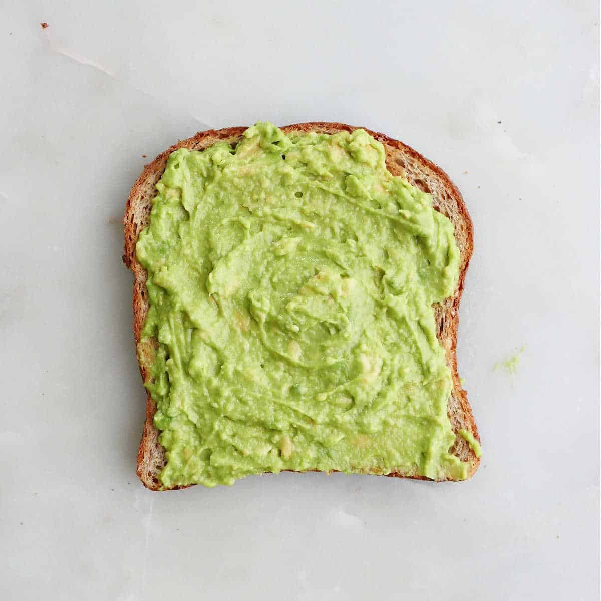 avocado spread onto a piece of toasted bread on a counter
