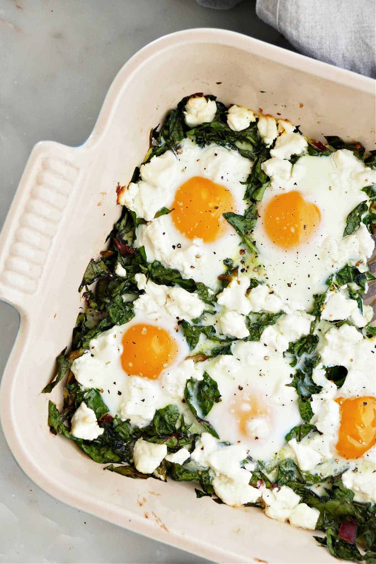 baked eggs with chard and goat cheese in a ceramic casserole dish on a counter