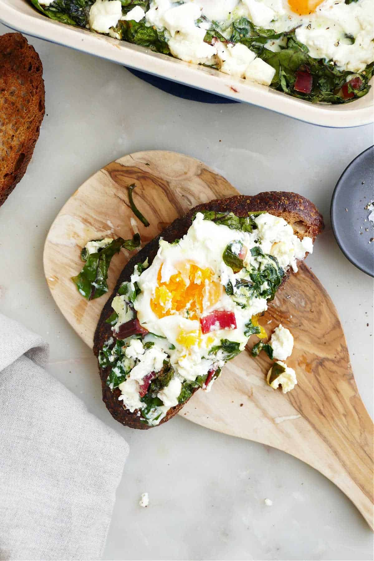 baked eggs, chard, and goat cheese on a slice of toast on a wooden board