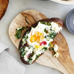 baked eggs, chard, and goat cheese on a slice of toast on a wooden board