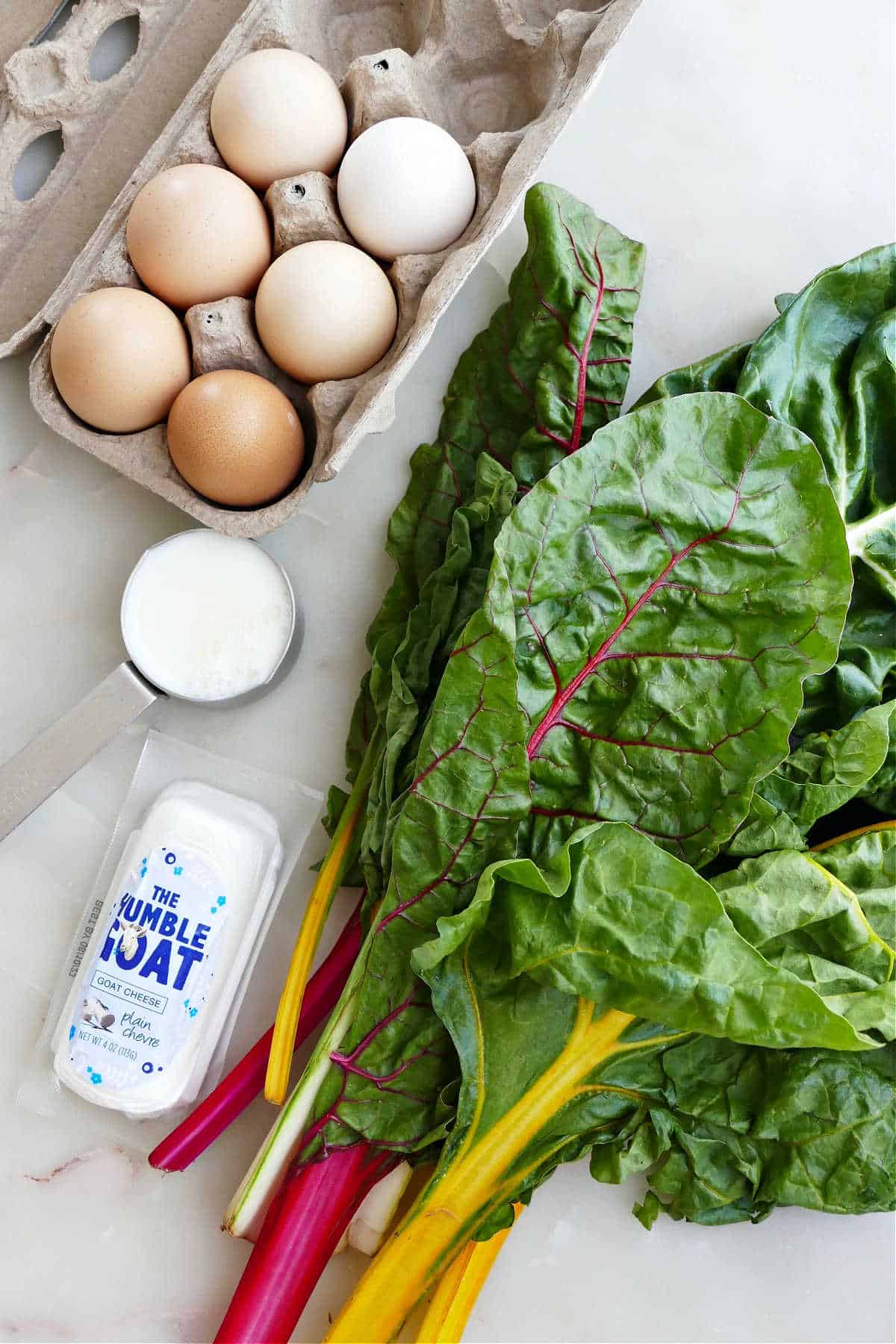 eggs, rainbow chard, goat cheese, and milk next to each other on a counter