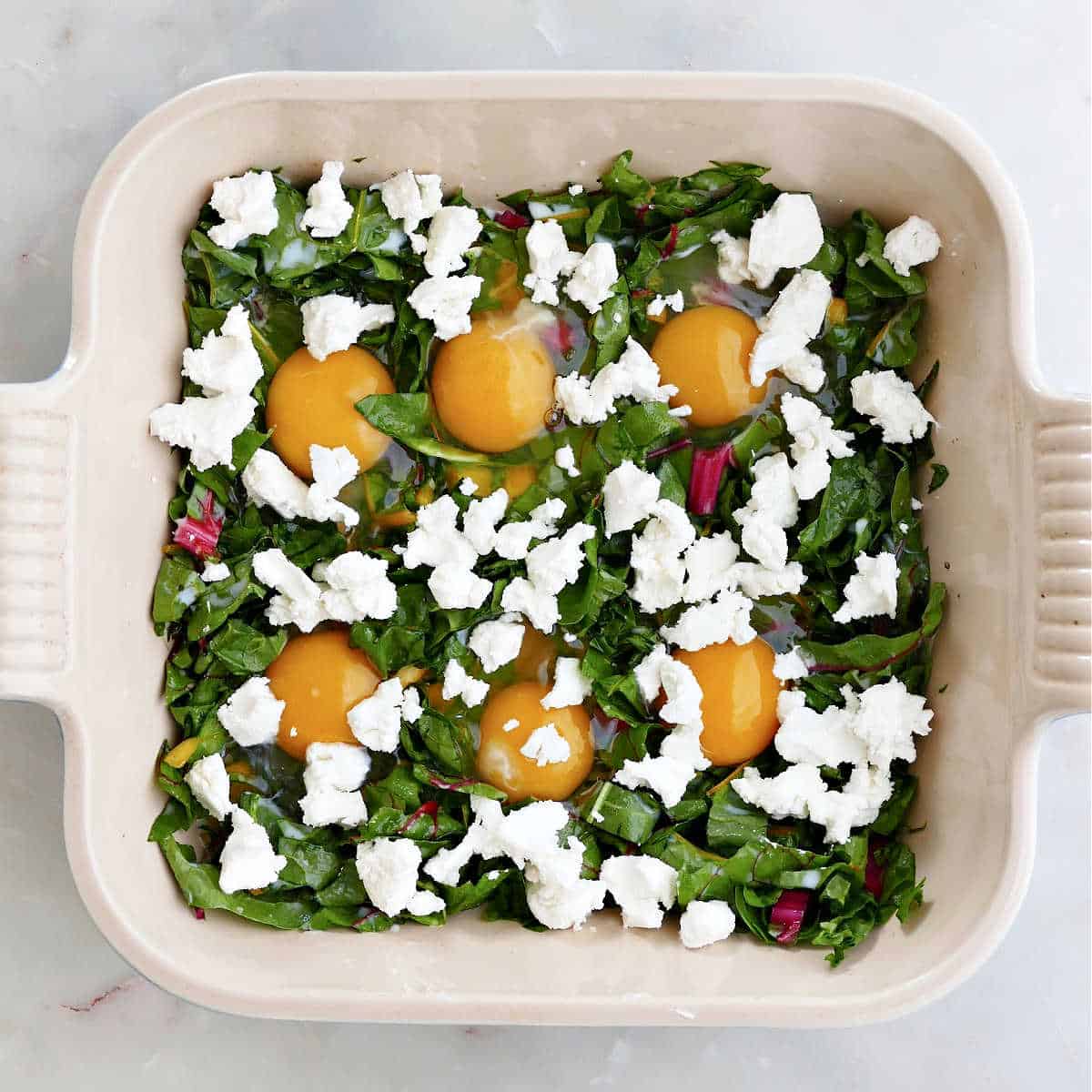 baked eggs and chard sprinkled with goat cheese in a dish before going into the oven