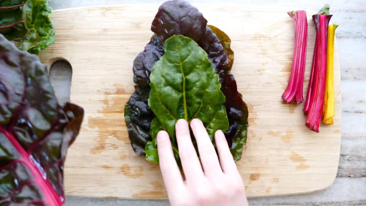 woman stacking chard leaves on top of each other on a cutting board