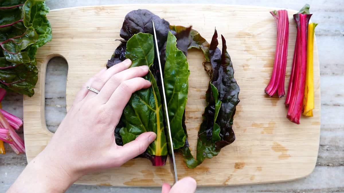 woman slicing chard lengthwise into strips on a cutting board
