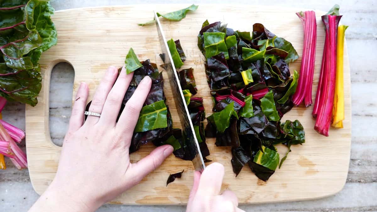 woman cutting strips of Swiss chard into pieces on a cutting board