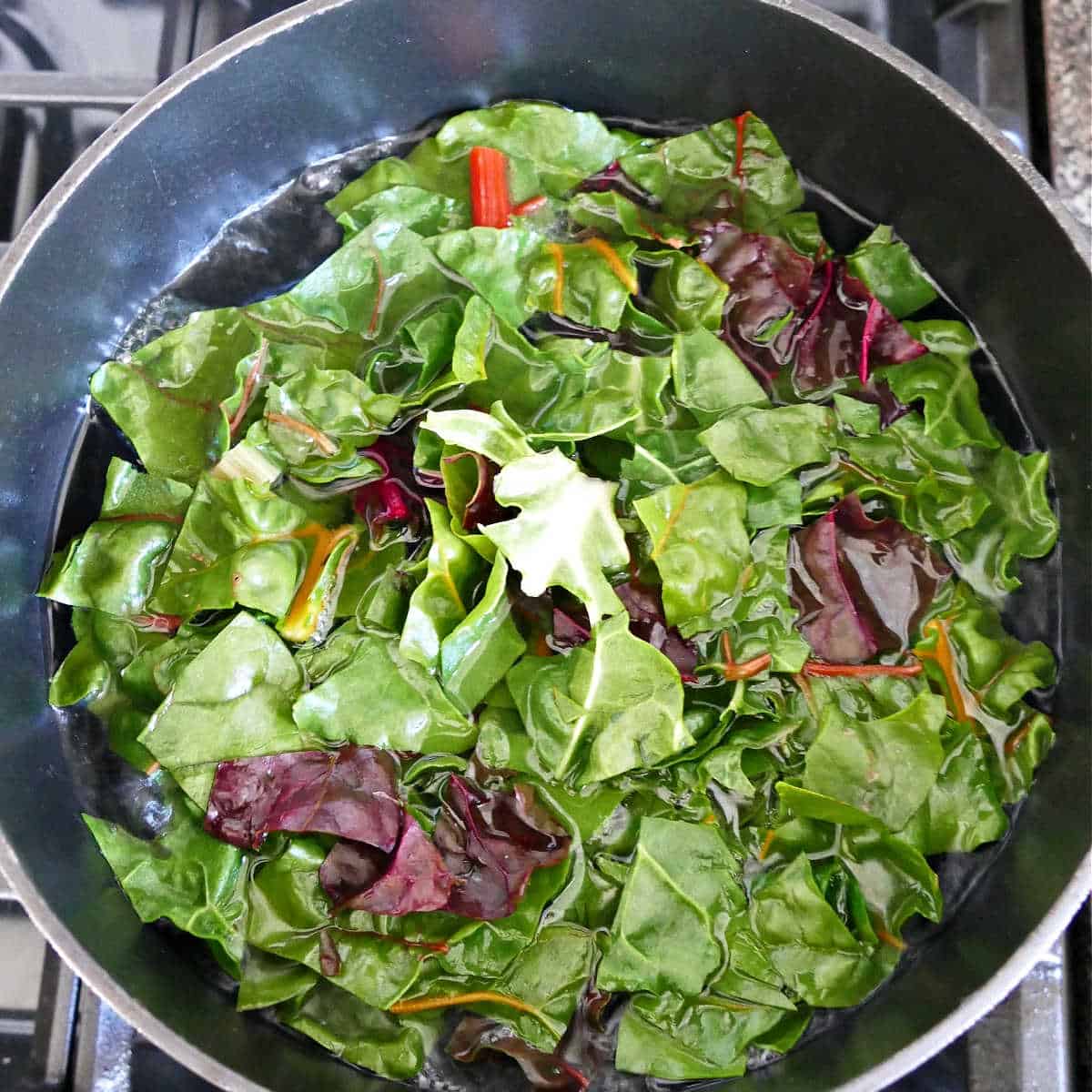 chard leaves being blanched in a pot of boiling water on the stove