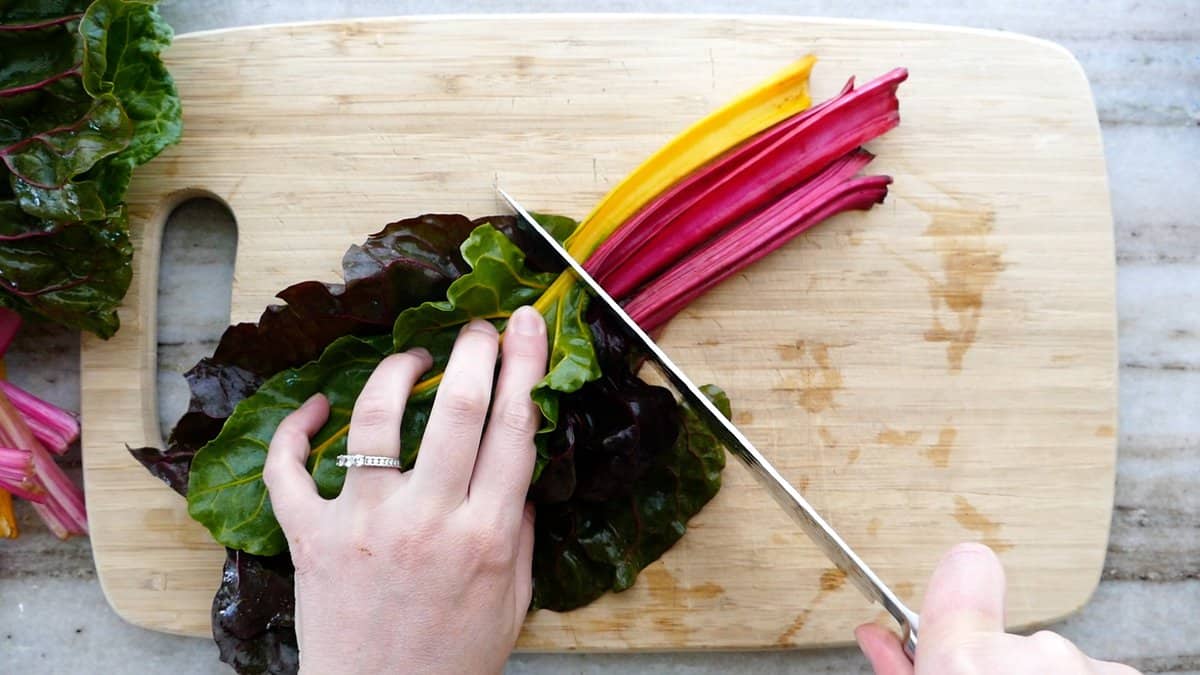 woman removing the stems of rainbow chard with a knife on a cutting board