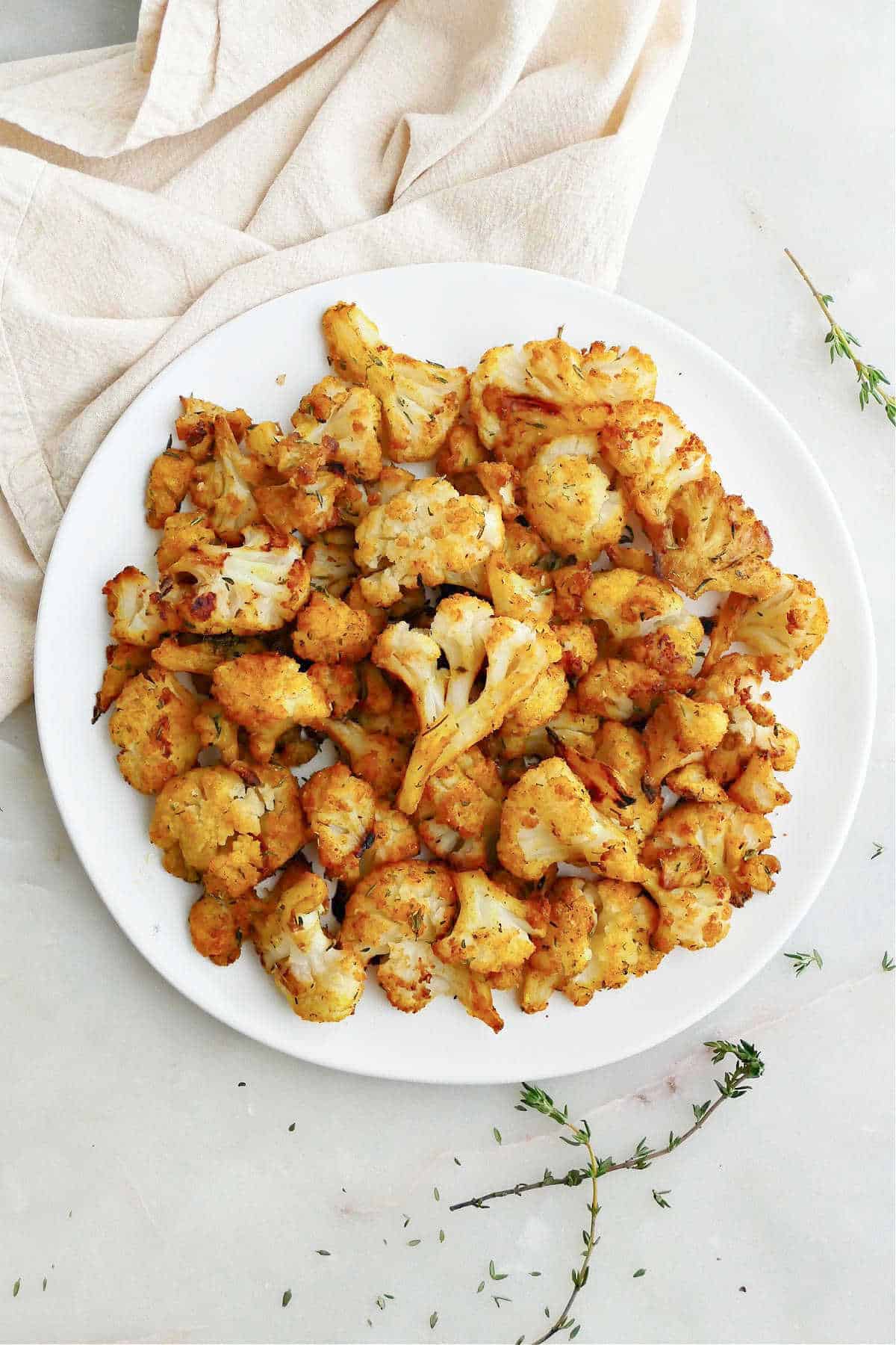 curry roasted frozen cauliflower on a serving plate next to napkin and thyme sprigs