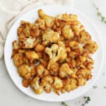 curry roasted frozen cauliflower on a serving plate next to napkin and thyme sprigs