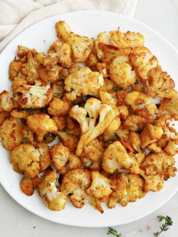 curry roasted frozen cauliflower on a serving plate next to napkin and thyme sprigs
