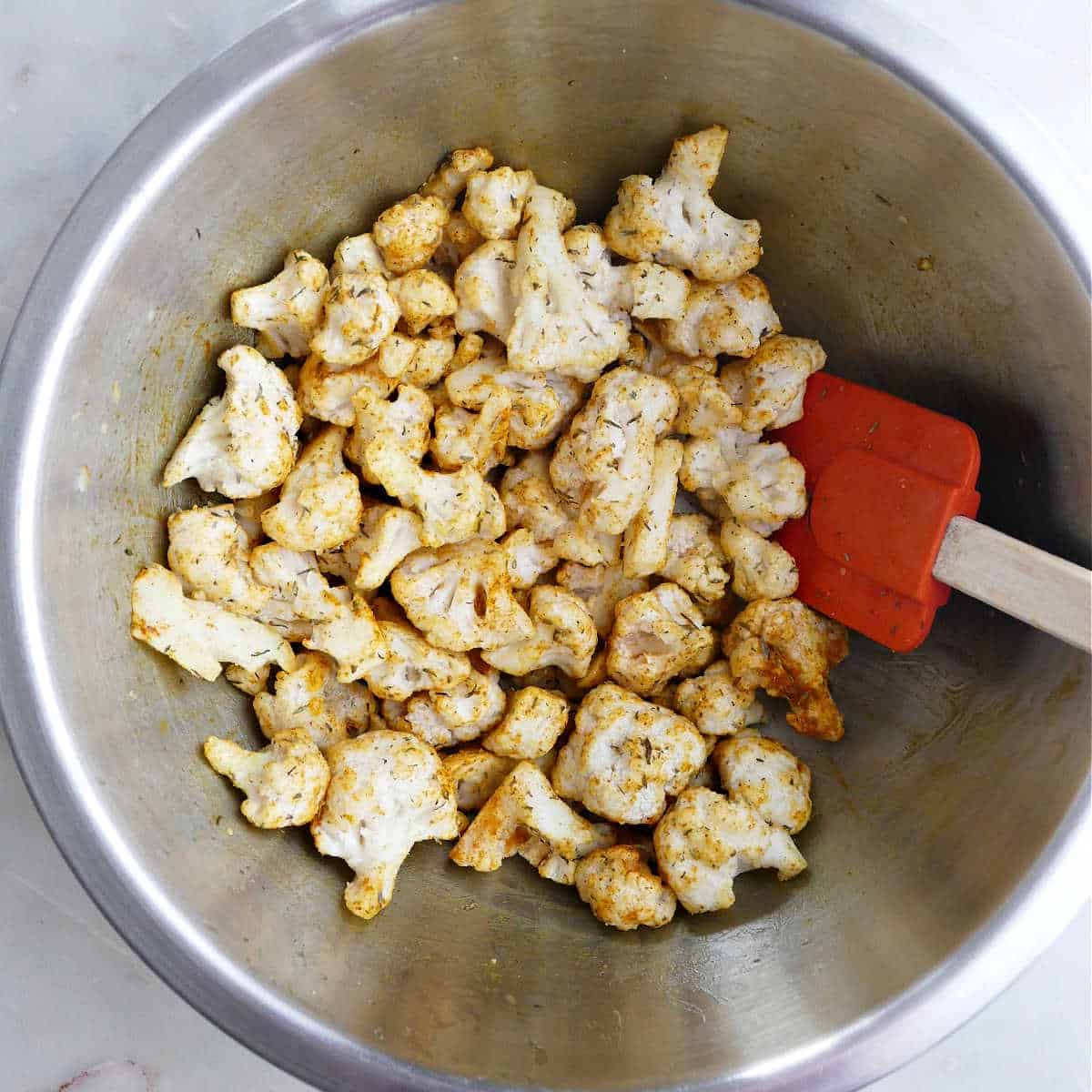 frozen cauliflower being tossed in olive oil and seasonings in a bowl