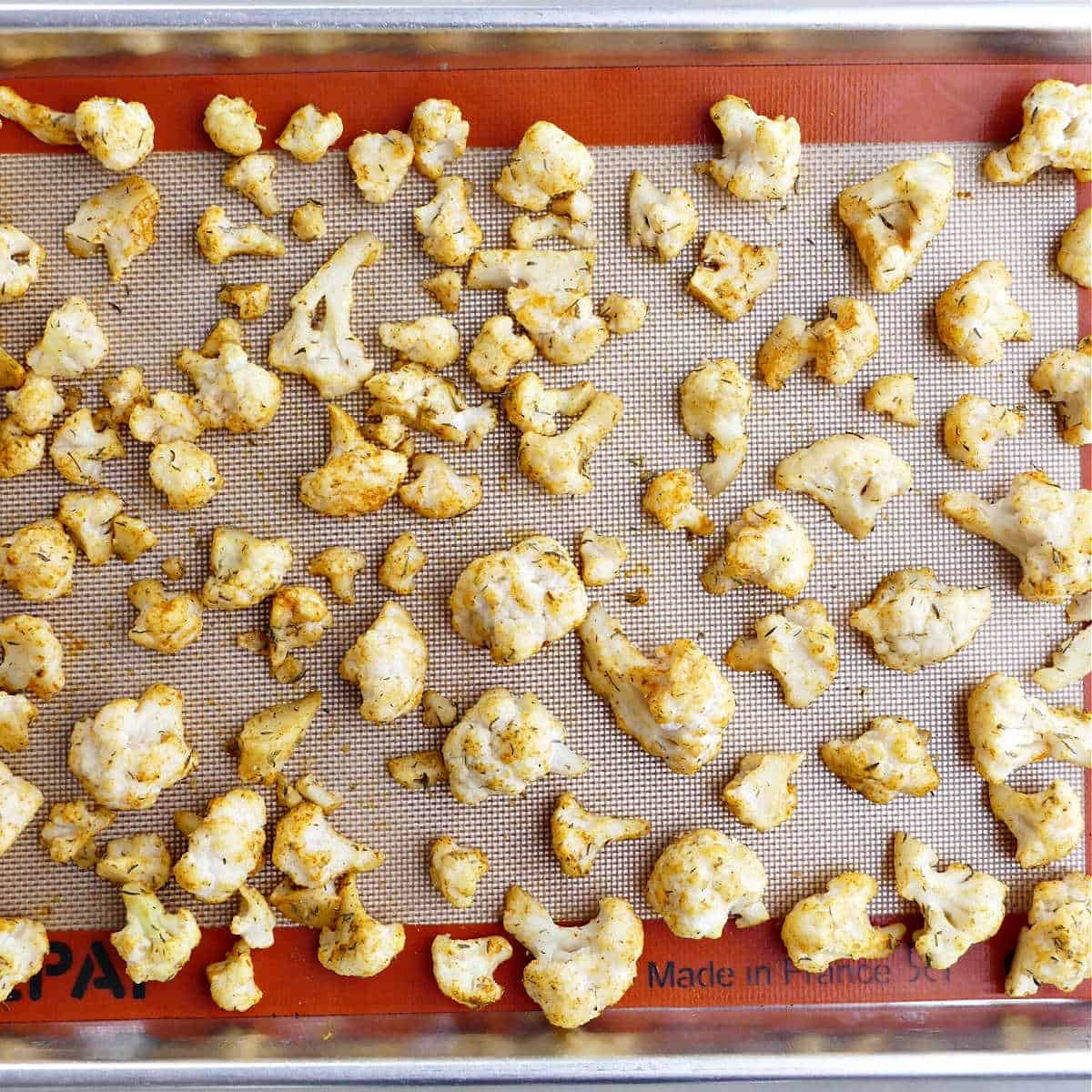 frozen cauliflower spread out on a lined baking sheet before being roasted in the oven