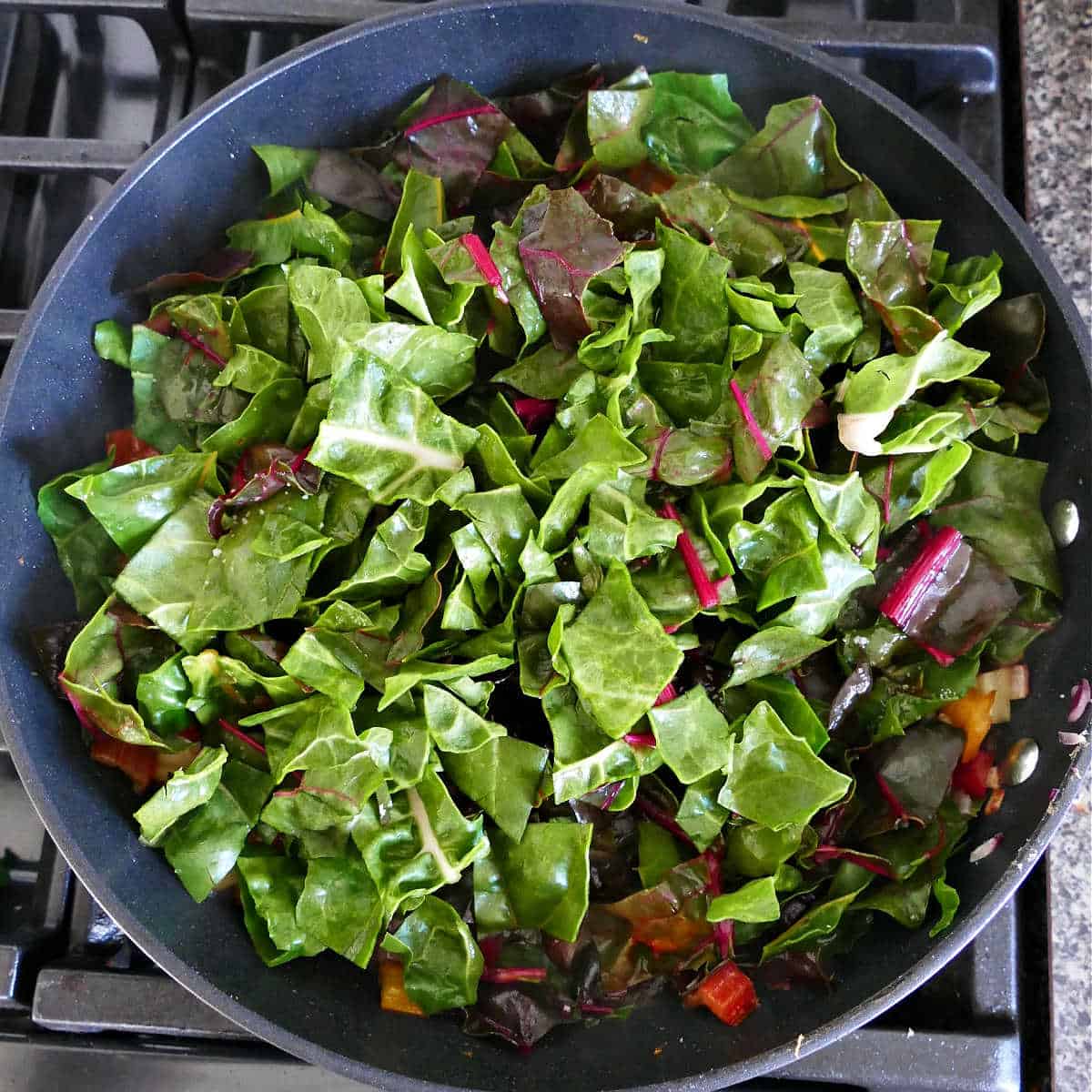 chard leaves added to a skillet with chard stems cooking in olive oil
