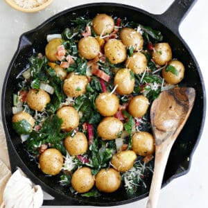 chard and potatoes with cheese in a cast iron skillet with a wooden spoon