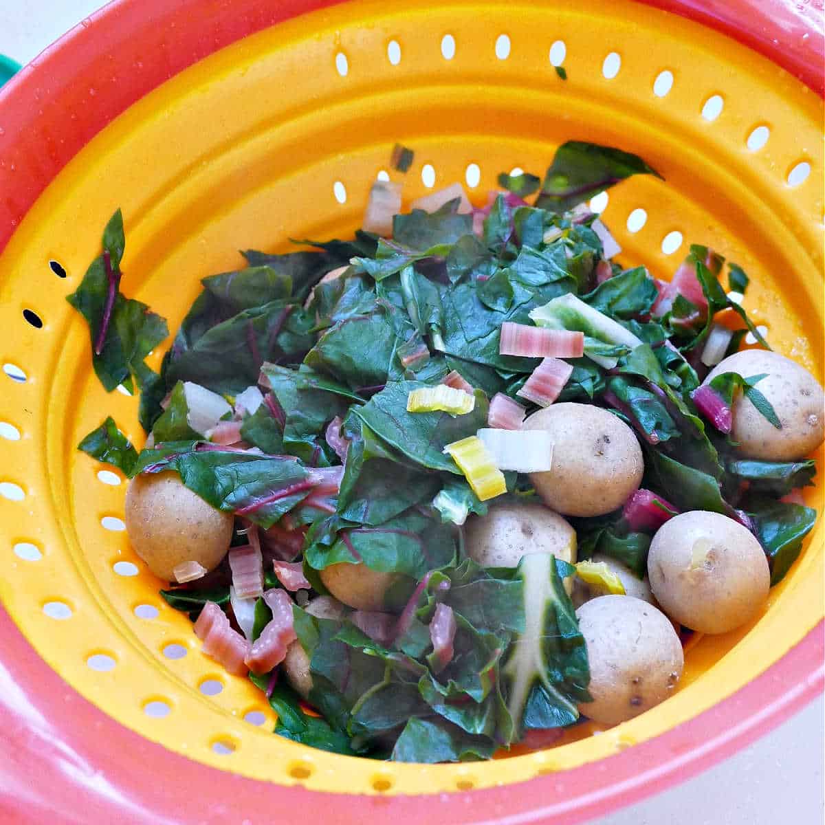 potatoes and chard being drained in a colander in a sink