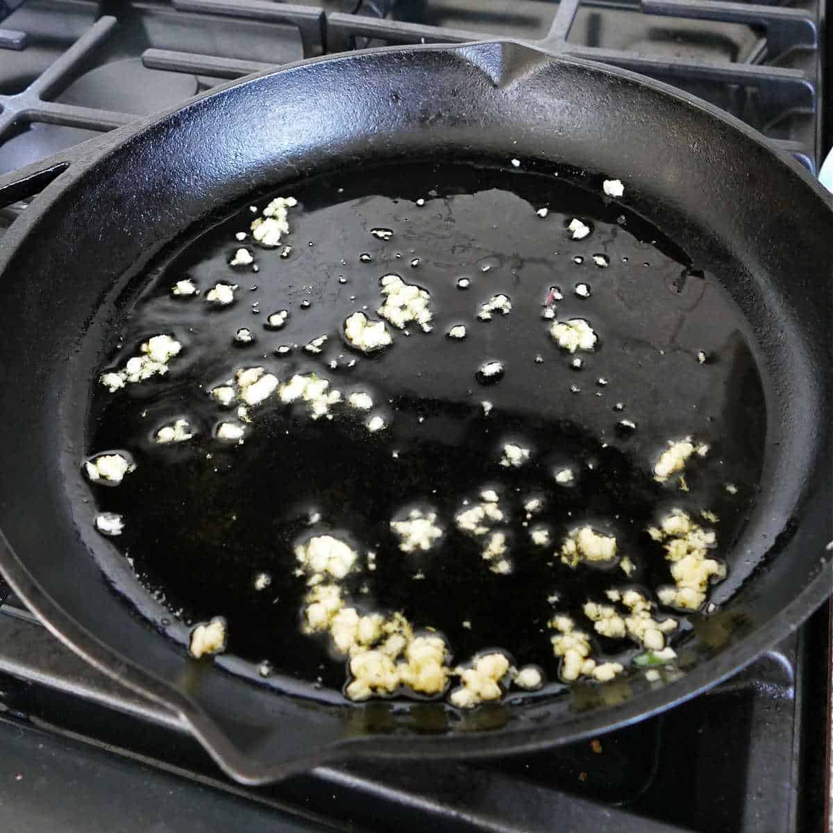 garlic cooking in olive oil in a skillet on the stove