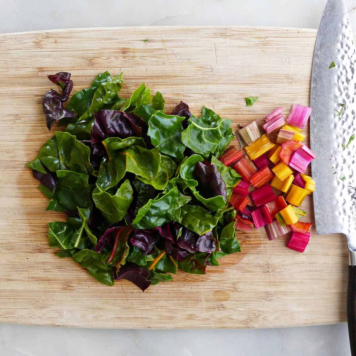 Swiss chard leaves and stems cut up on a cutting board with a knife