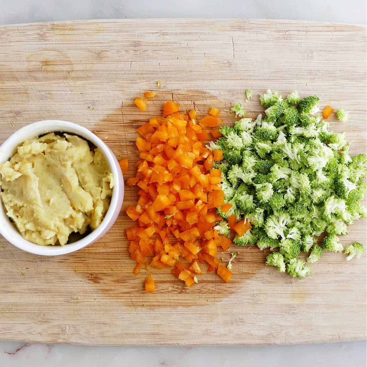 mashed potatoes and diced vegetables on a cutting board on a counter