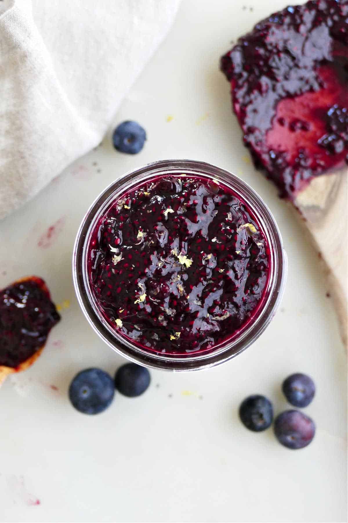 blueberry chia jam in a jar on a counter surrounded by berries and tools