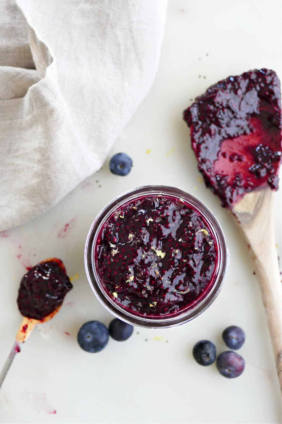 blueberry chia jam in a jar on a counter surrounded by berries and tools