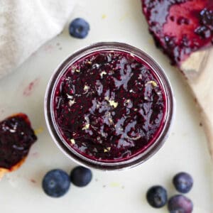 blueberry chia jam in a jar on a counter surrounded by berries and tools