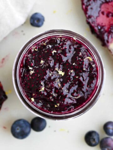 blueberry chia jam in a jar on a counter surrounded by berries and tools