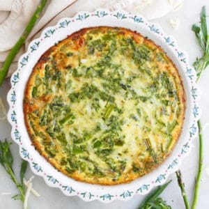 crustless asparagus quiche in a pie plate topped on a counter surrounded by ingredients