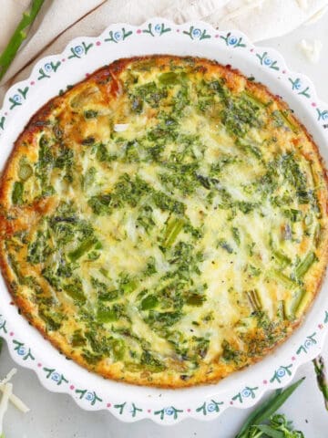 crustless asparagus quiche in a pie plate topped on a counter surrounded by ingredients