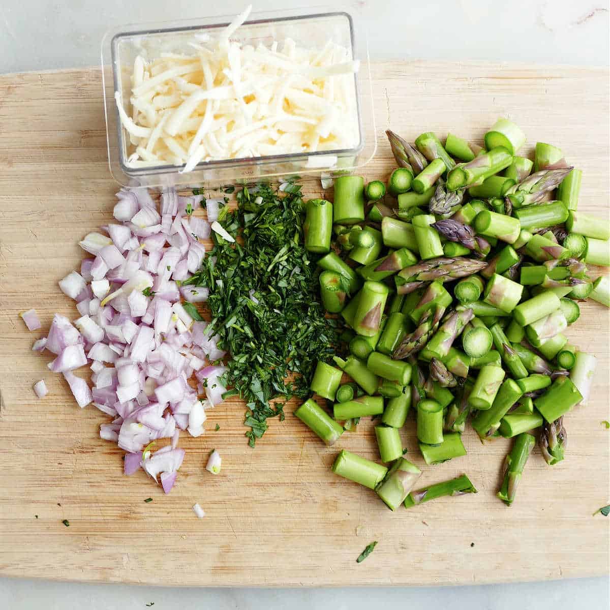 diced shallot, tarragon, and asparagus on a cutting board next to grated cheese