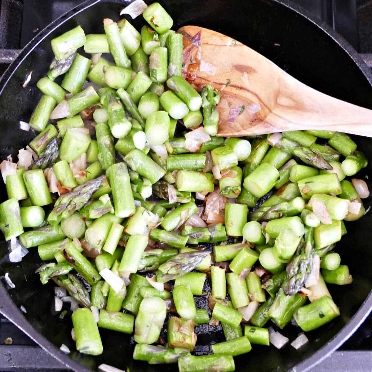 asparagus cooking with shallots in olive oil in a skillet