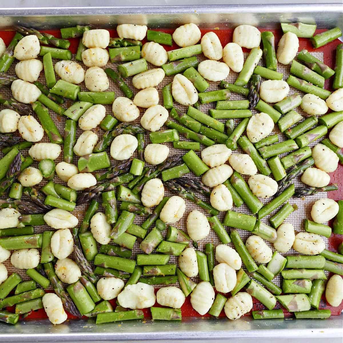 asparagus and gnocchi spread out on a baking sheet lined with a silicone mat