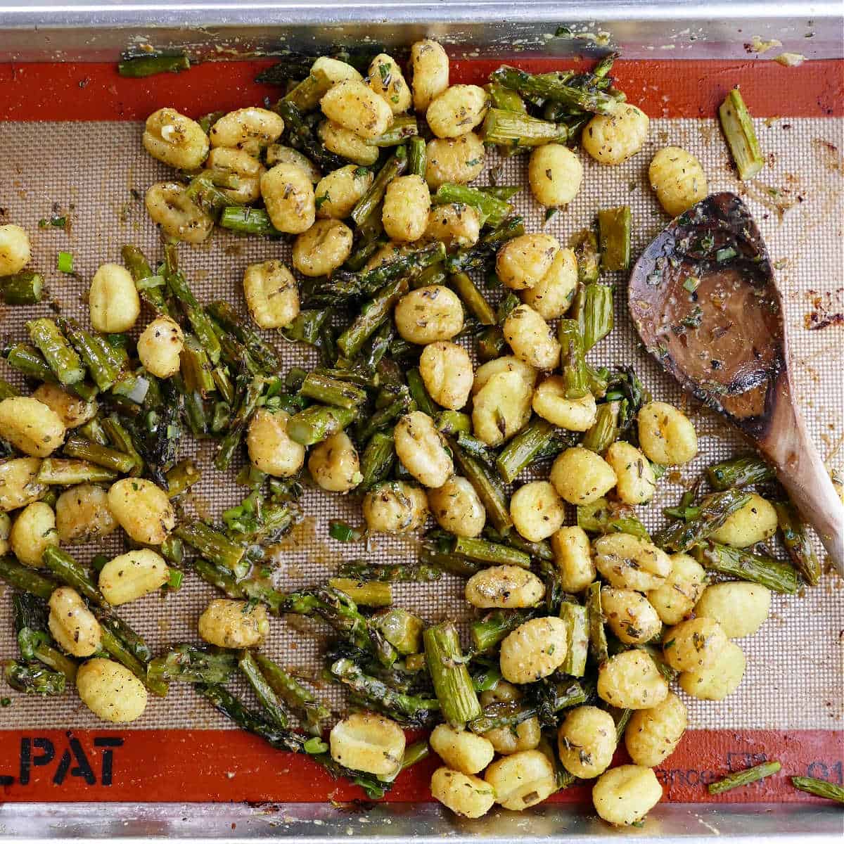 gnocchi and asparagus baked on a lined sheet pan with a spoon