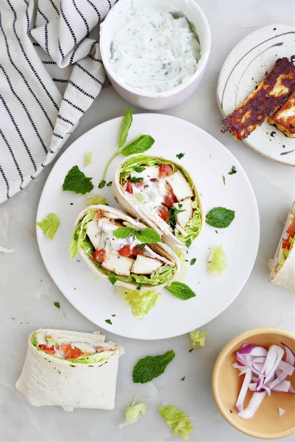 halloumi wrap sliced in half on a serving plate surrounded by ingredients