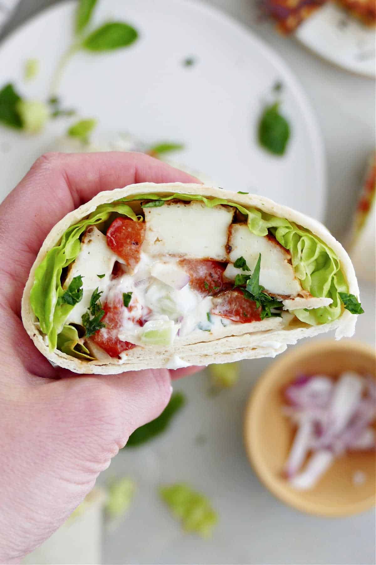 half of a halloumi and vegetable wrap with yogurt sauce in a woman's hand