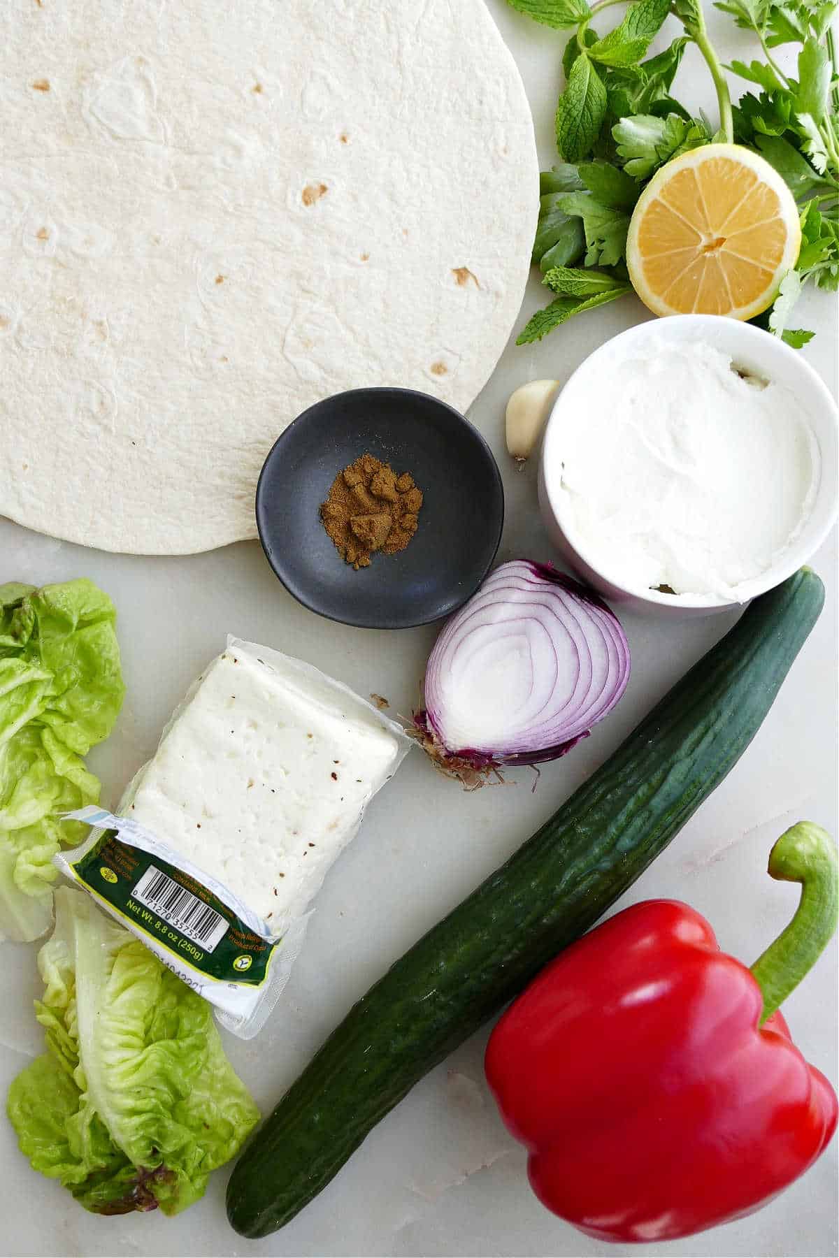 large tortillas, vegetables, halloumi cheese, yogurt, lemon, and seasonings on a counter