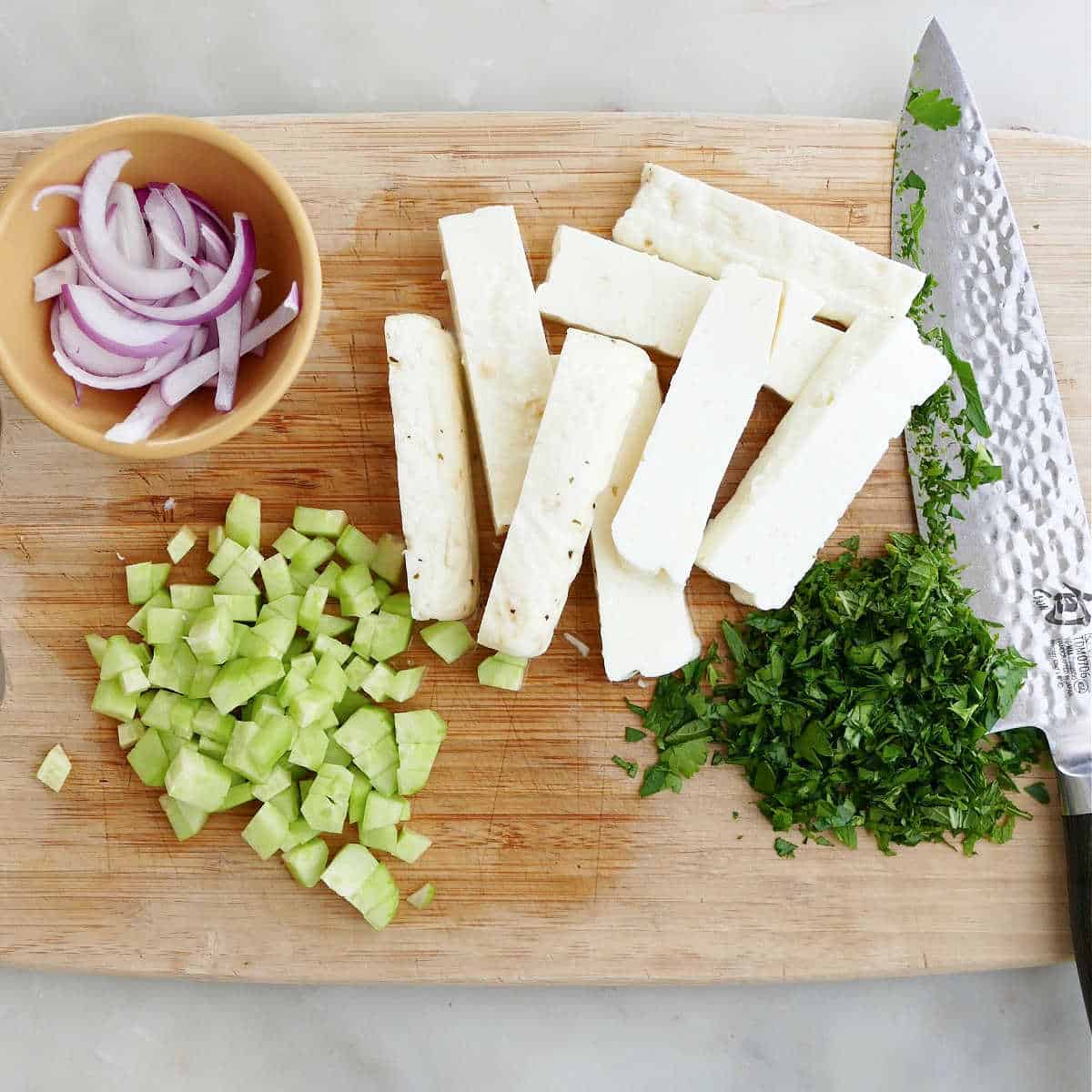 chopped vegetables and sliced halloumi cheese on a cutting board